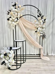 a wedding arch decorated with white flowers and black accents, along with two side tables