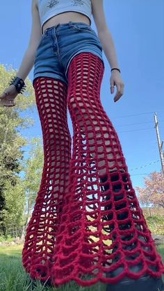 a woman is standing in the grass wearing red crochet pants and high heels