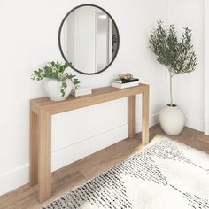 a wooden table with a mirror and potted plant on it in front of a white wall