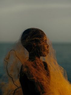 a woman standing in front of the ocean with her hair blowing in the wind and looking off into the distance