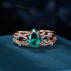 a ring with an emerald colored stone and leaves on the sides, sitting on a blue cloth