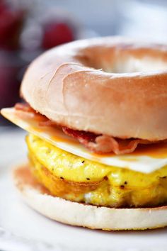 a bagel sandwich with eggs, bacon and cheese on it sitting on a plate