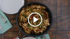 a skillet filled with food on top of a wooden table next to plates and utensils