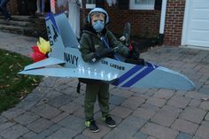 a young boy wearing a mask and holding a toy airplane on the sidewalk in front of a house