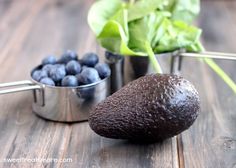 an avocado, blueberries and spinach are sitting on a wooden table