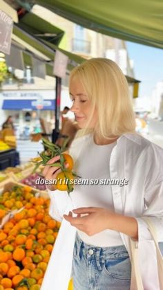 a woman standing in front of a fruit stand looking at her cell phone while holding an orange