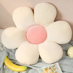 a flower shaped pillow sitting on top of a bed next to bananas and an apple