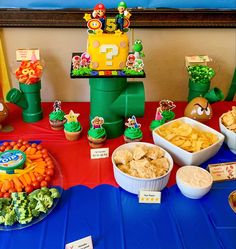 a table topped with lots of food next to cupcakes and other items on top of a blue table cloth