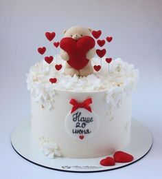 a teddy bear sitting on top of a white cake covered in frosting and hearts