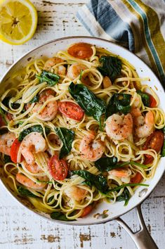 pasta with shrimp, spinach and tomatoes in a skillet on a white wooden table