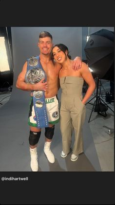 a man and woman standing next to each other in front of a photo studio holding a wrestling belt