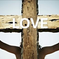 a cross with the word love painted on it and someone's hands behind it