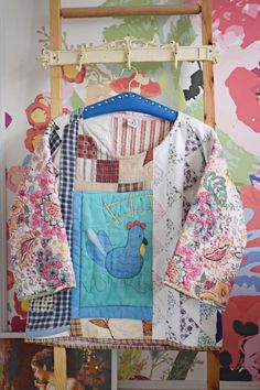 a quilted jacket hanging on a wooden ladder in front of a wall with flowers