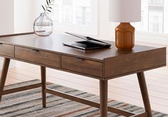 a wooden desk with a lamp on it and a book in front of the table