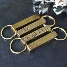 four gold key chains with roman numerals on them and flowers in the background