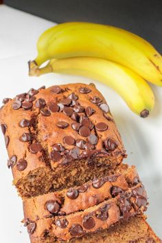 two slices of chocolate chip banana bread on a white plate next to some ripe bananas