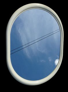 a round mirror with power lines in the background and clouds in the sky behind it