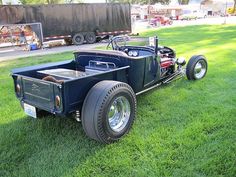 an antique car is parked on the grass in front of a large truck and trailer