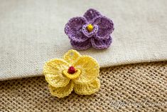 two crocheted flowers sitting on top of a piece of burlock fabric