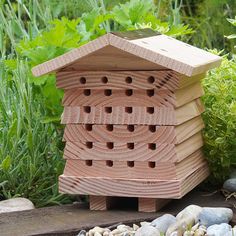 a wooden bee house sitting on top of a rock covered ground next to plants and rocks