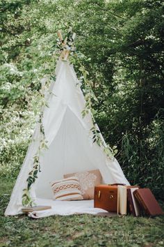 a teepee in the woods with books and plants on it, next to an open book