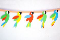 paper parrots are hanging on a string with orange tape and blue, green, red, yellow and black feathers