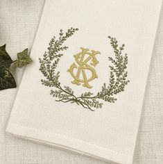 an embroidered monogram on a linen napkin next to some ivy leaves and a leafy twig