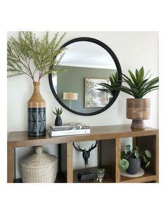 there is a mirror on the wall above a shelf with plants and vases next to it