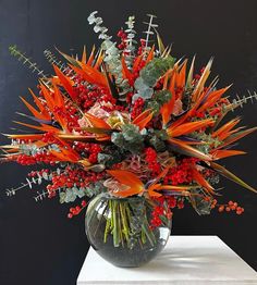 a vase filled with lots of red flowers and greenery on top of a white table