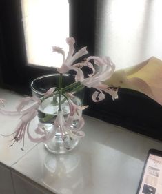 there is a vase with flowers in it and a cell phone on the table next to it