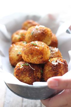 a person holding a bowl filled with fried meatballs and garnished with parsley