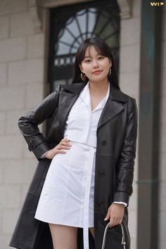 a woman in white shirt dress and black trench coat posing for the camera with her hand on her hip