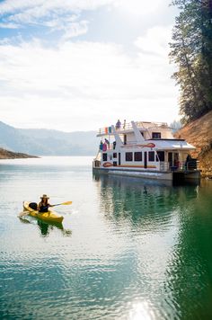 a person in a yellow kayak paddling on the water near a houseboat