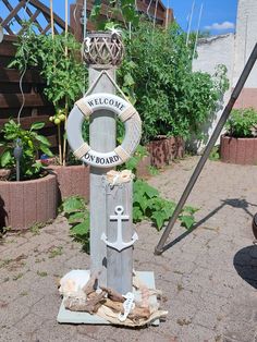 a welcome sign with an anchor and life preserver in the middle of a garden