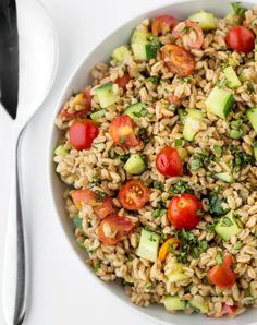 a white bowl filled with rice, cucumbers and tomatoes next to a fork