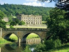 an old stone bridge over a river in front of a large building on a hill