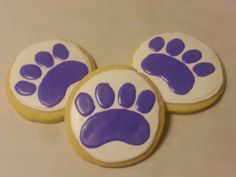 three decorated cookies with purple and white paw prints