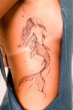 a woman's back with a tattoo design on her arm and the image of a mermaid