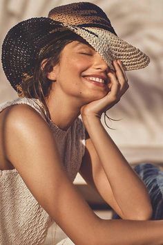 a woman sitting on the ground with her eyes closed and wearing a straw hat over her head