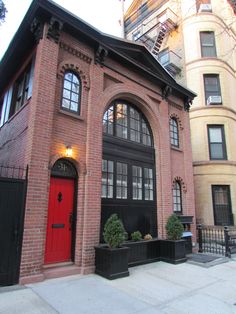 an old brick building with a red door and black planters on the sidewalk in front of it