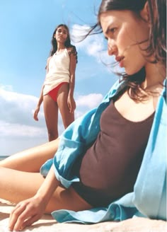 two young women sitting on the beach with their legs spread out in front of them