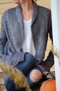 a woman is sitting on the porch with her legs crossed and wearing ripped jeans, a gray cardigan sweater and white t - shirt