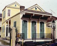 an old yellow house with green shutters on the front and side windows, next to a black car