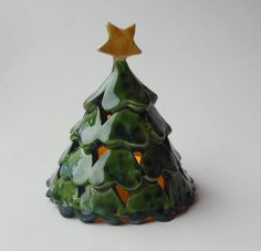 a small green ceramic christmas tree with a star on it's top, sitting in front of a white background