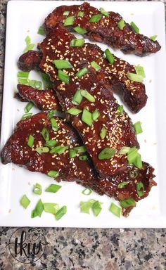 some meat with green onions and sesame seeds on a white platter, ready to be eaten