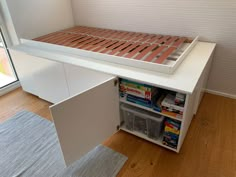 an open drawer underneath a bed in a room with wood flooring and white walls