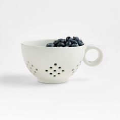 a white bowl filled with blueberries sitting on top of a table next to a cup