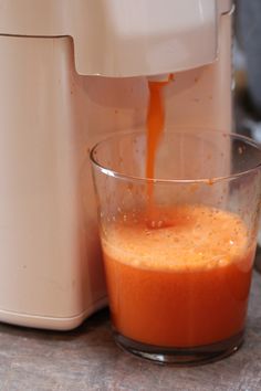 orange juice being poured into a glass in front of an electric blender on a counter