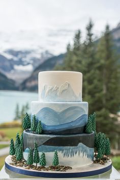 a three tiered cake with mountains and trees on it is sitting on a table