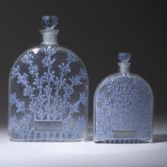 two glass bottles with designs on them sitting next to each other in front of a gray background